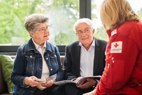 Eine ältere Frau und ein älterer Mann im Gespräch mit einer Rot-Kreuz-Mitarbeiterin